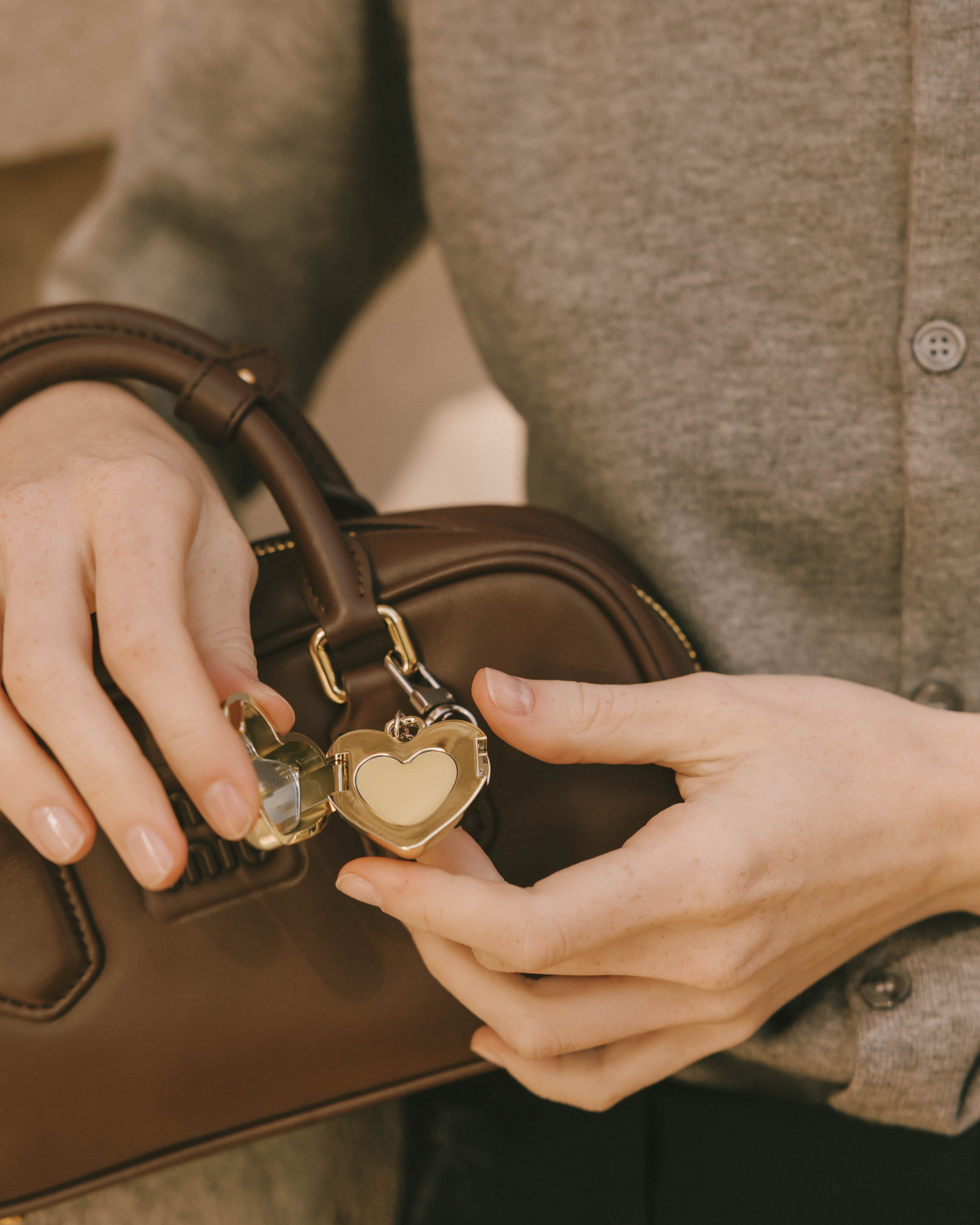 a woman opened a gold heart-shaped perfume balm keychain charm attached to the bag.
