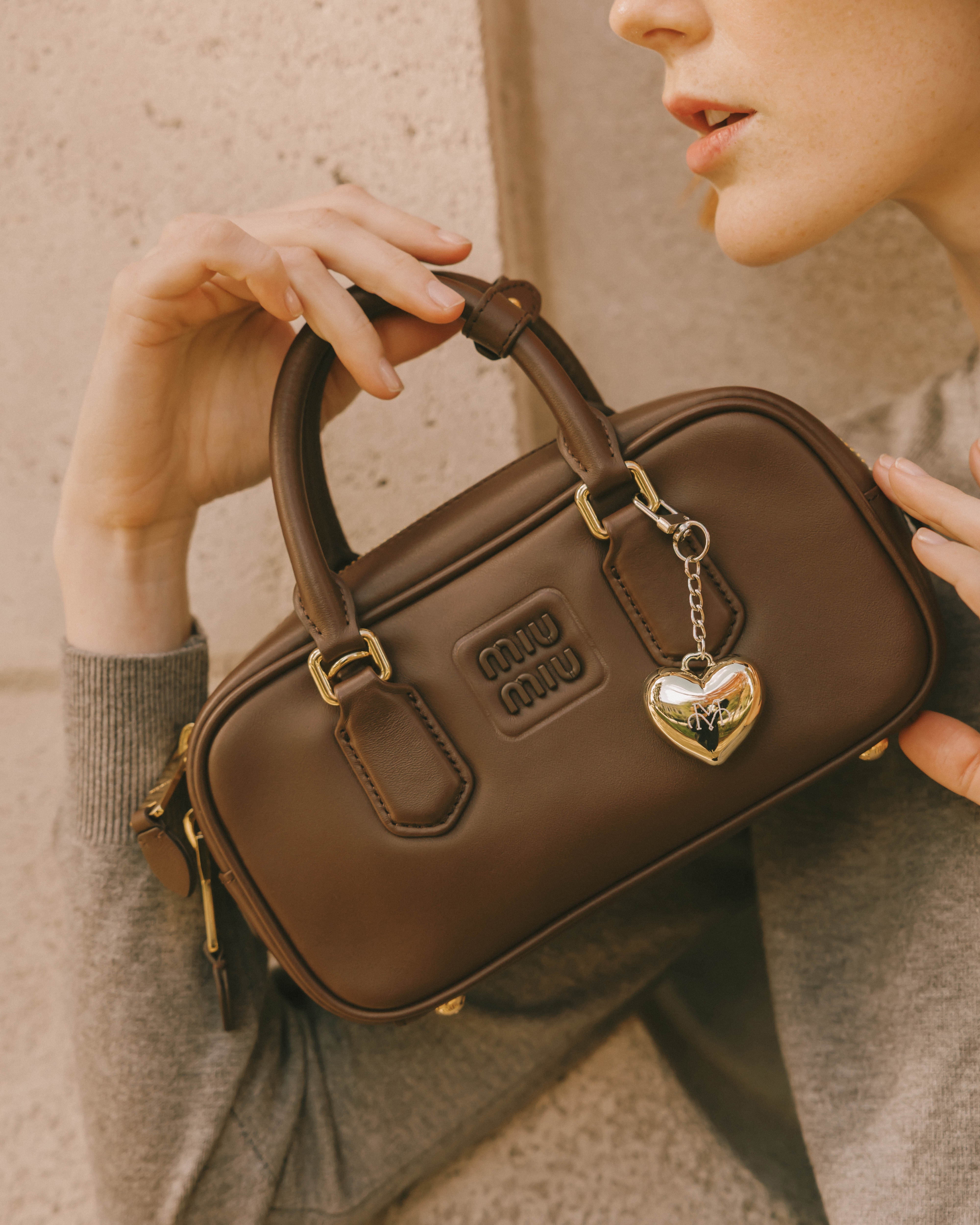a women is holding a brown bag with a perfume balm bag charm which is perfect for travelling. 